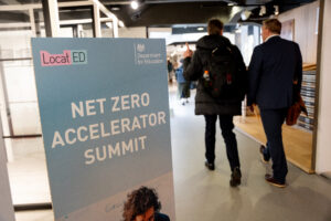 Two delegates walking past a sign for the Net Zero Accelerator Summit into the venue